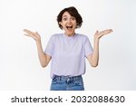 Small photo of Image of excited and surprised brunette woman gasp fascinated, spread hands sideways and looking speechless impressed, rejoicing, being happy for someone, white background