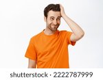 Small photo of Portrait of confused man, scratching head and looking complicated, being questioned, standing in orange tshirt over white background.