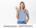 Small photo of Perfect, very good. Smiling attractive young woman showing okay, ok gesture and looking satisfied, recommending great product, praise or approve smth, white background