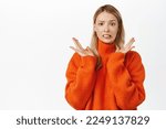 Small photo of Confused and embarrassed young blond woman cringe, smiling awkward, looking at smth unpleasant or disgusting, standing over white background