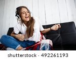 Girl in plaid listening music in headphones, sitting on sofa.