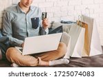 Closeup young happy man sit on couch, using laptop for safe online shopping from home. Stylish male hipster shopper hold credit card in hand. Payments and purchases at internet store. Man shopaholic
