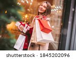Beautiful happy girl hold shopping bags and gift boxes in hands and smile on city street. Young attractive cheerful woman with paper bags and present box after Christmas shopping in mall. Winter sale
