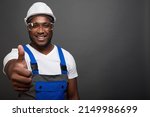 Small photo of An African-American construction worker shows a thumbs up in the final stage of the reconstruction of the facility. Happy black worker in helmet and goggles with a close-up gesture of admiration