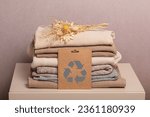 Small photo of Stack of second hand clothes with used wardrobe for reuse and card with circular economy logo. Reusing, recycling materials and reducing waste in fashion, second hand apparel idea. Zero waste concept