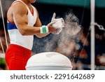 close-up hands male gymnast in gymnastics grips apply gym chalk from magnesia stands
