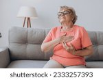 Small photo of Senior woman with pain on heart in living room, older female presses hand to chest has heart attack suffers from unbearable pain