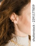 Small photo of Cropped close-up shot of a young woman with two asymmetrical golden ear cuffs. Female with golden ear cuffs, side view.