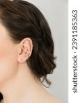 Small photo of Cropped close-up shot of a young woman with asymmetrical silver ear cuffs. Female with metal ear cuffs, side view