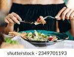 Holding pieces of caesar salad with fork and knife in female hands over blue plate with food on female silhouette background