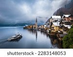 Hallstatt, Austria - Iconic view of world famous Hallstatt, the Unesco protected lakeside town with Hallstatt Lutheran Church on a cold foggy day with traditional passenger ship and snowy rooftops