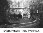 pathway out of cemetery. Cemetery gate with arc and catholic cross, give way road sign and old abanoned building outside graveyard. Black and white with red color left