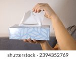 Small photo of Close up of woman's hands holding a tissue box and a nose spry bottle, white blurry background