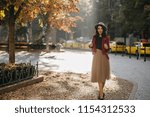 Full-length portrait of enchanting brunette girl standing on the street in sunny day. Outdoor shot of slim pleased lady in long skirt enjoying nature views in autumn.