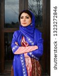 Small photo of Beautiful azeri woman in traditional Azerbaijani dress standing at the wooden window outdoors. Novruz holiday celebration