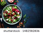 Arugula, Beet and cheese salad with fresh radicchio and walnuts on plate with fork, dressing and spices on blue kitchen table background, place for text, top view