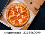 Small photo of Pepperoni pizza in box with spicy salami sausage, mozzarella cheese, tomato sauce, just delivered,, black table background, top view
