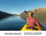 Beautiful woman enjoying her yellow kayak on the lake and overlooking the mountains. Well deserved summer vacation. Patagonia, Argentina.