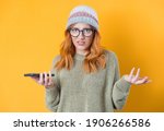 Small photo of Confused cute woman holding the phone, isolated on yellow background. Female with smartphone. Nuisance concept. Studio shot