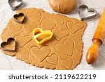 Process of making heart-shaped gingerbread for Valentine's Day. Cutting hearts out of dough with cookie-cutters. Dough, rolling pin and cookie cutters on table