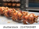 Small photo of front view of four whole roasted chickens, a rotisserie machine in the background
