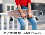 Unrecognized young woman holding longboard in the street and wearing casual clothes.