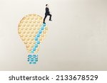 European man in suit standing on abstract pattern light bulb on light background with mock up place. Idea, growth and success concept