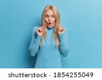 Small photo of Stunned blonde young pretty European woman stands impressed looks with bated breath opens mouth in amazement wears casual clothes isolated over blue studio background. Human reactions concept
