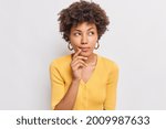 Horizontal shot of thoughtful young African American woman looks aside has dreamy expression interesting idea in mind wears casual yellow jumper isolated over white background makes decision