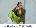 Horizontal shot of beautiful teenage girl with trendy hairstyle dressed in green clothes looks away poses against urban grey wall considers something. People youth lifestyle and fashion concept