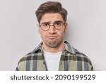 Small photo of Portrait of sad unhappy man frowns face upset with bad news he received wears round spectacles and casual checkered shirt isolated over white background feels reluctant. Negative emotions concept