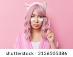Small photo of Sad upset rosy haired young Asian woman wakes up early in morning applies white beauty patches under eyes olds toot brush undergoes undergoes daily hygiene routines poses against pink background.