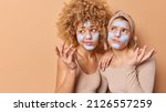 Small photo of Hesitant confused young women shrug shoulders feel unaware apply beauty mask face difficult question stand against beige background blank space away for your advertising content Wellness concept