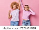 Small photo of Two friendly girls have fun dance carefree shake arms chill together have glad expressions foolish around dressed in casual clothes isolated over pink background. People and entertainment concept