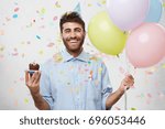 People, joy, fun and happiness concept. Relaxed happy birthday guy looking cheerful, smiling happily, posing for picture, holding colorful helium balloons and cupcake with confetti falling down