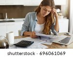 Indoor shot of casually dressed young woman holding papers in her hands, calculating family budget, trying to save some money to buy new bicycle to her son, having stressed and concentrated look