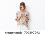 Small photo of Horizontal portrait of happy smiling female with bobbed hairstyle dressed casually being happy to recieve invitation for birthday party from friend, typing answer, promising necessarily to come