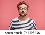 Funny male with curly trendy hairstyle, rounds lips as going to kiss someone, looks in anticipation, isolated over pink background. Fashionable bearded man epresses positive emotions, makes grimace