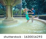 A couple dancing in a fountain in a park surrounded by greenery under sunlight