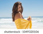 Cheerful young woman in yellow sarong at beach. Happy smiling girl enjoying the beach and looking at camera. Latin tanned woman feeling refreshed in yellow scarf during summer vacation.