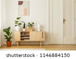 Retro style, wooden sideboard with green plants and a poster on a white wall in a simple apartment interior with herringbone hardwood floor. Real photo.
