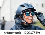 An active senior woman with bike helmet standing outdoors, putting on sunglasses.
