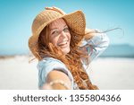 Portrait of beautiful mature woman in casual wearing straw hat at seaside. Cheerful young woman smiling at beach during summer vacation. Happy girl with red hair and freckles enjoying the sun.