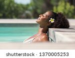 Young black woman relaxing at spa pool. Beautiful woman relaxing in outdoor spa swimming pool with head leaning at poolside. Closeup face of attractive girl with closed eyes enjoy vacation at resort.
