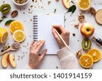Female hand write in notebook on healthy food background, women diet nutrition recipe menu, fresh summer fruit granola seeds on white table organic super food, health care detox, top view, copy space