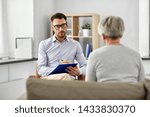 geriatric psychology, mental therapy and old age concept - psychologist with clipboard taking notes and listening to senior woman patient at psychotherapy session