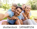 family, leisure and technology concept - happy mother, father and two little sons having picnic and taking selfie at summer park