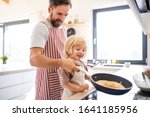 A side view of small boy with father indoors in kitchen making pancakes.