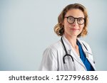 Portrait of happy mid adult smiling doctor looking at camera. Happy beautiful mature pediatrician standing over blue background with copy space. Reliable general practitioner woman with stethoscope.