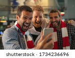 Excited men watching football in streaming on smartphone. Football fans watching game on phone and celebrating victory score at pub. Happy supporters cheering and exulting after winning an online bet.